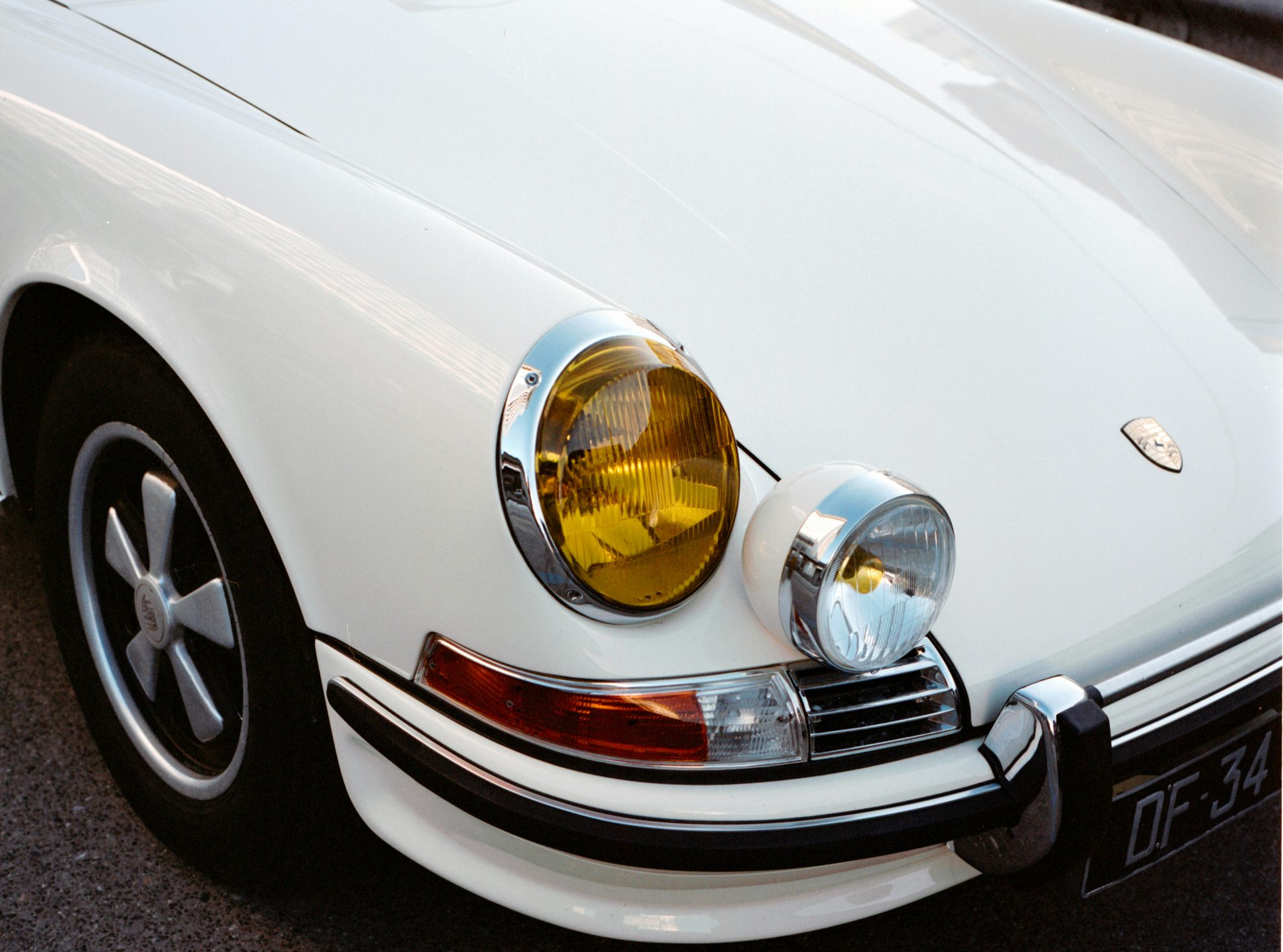 Close-up of a classic white Porsche 911 front, highlighting the iconic round headlights with one yellow-tinted and one clear.
